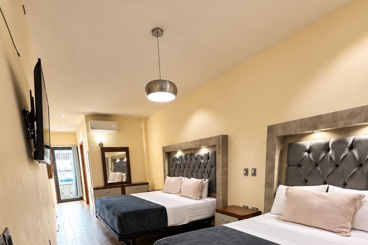 Une chambre d’hôtel avec deux lits, une télévision, un miroir et un luminaire au plafond.