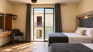 A hotel room with a bed, a desk, a chair, and a view of a balcony with flowers.