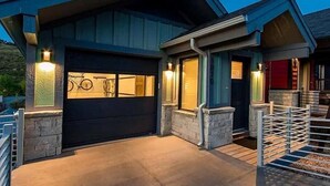 Une maison moderne à deux étages, dotée d’une porte de garage sombre, de piliers en pierre et d’une porte rouge.