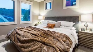 Une chambre à coucher avec un grand lit, deux tables de chevet, une commode et une fenêtre donnant sur une route et des collines.
