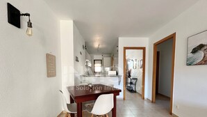 A dining area with a wooden table and chairs, a kitchen in the background, and a hallway leading to another room. - Regata green areas with swimming pools  (Cambrils)