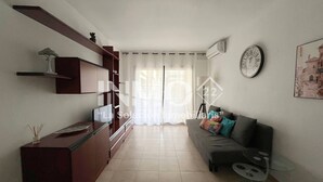 A modern living room with a sofa, a coffee table, and a TV. There is a bookshelf and a lamp. - Regata green areas with swimming pools  (Cambrils)