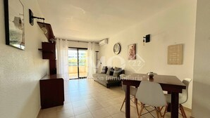 A spacious living area with a sofa, dining table, and chairs. There is a staircase leading to an upper floor, and a large window with curtains. - Regata green areas with swimming pools  (Cambrils)