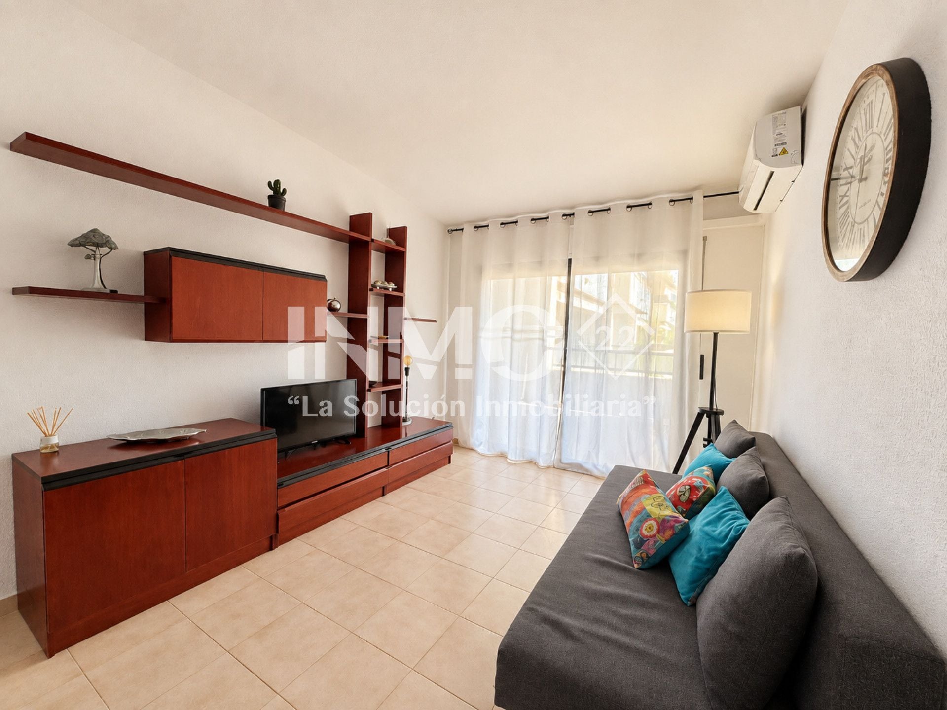 Una sala de estar moderna con un sofá, televisor, armarios de madera y un reloj en la pared.
