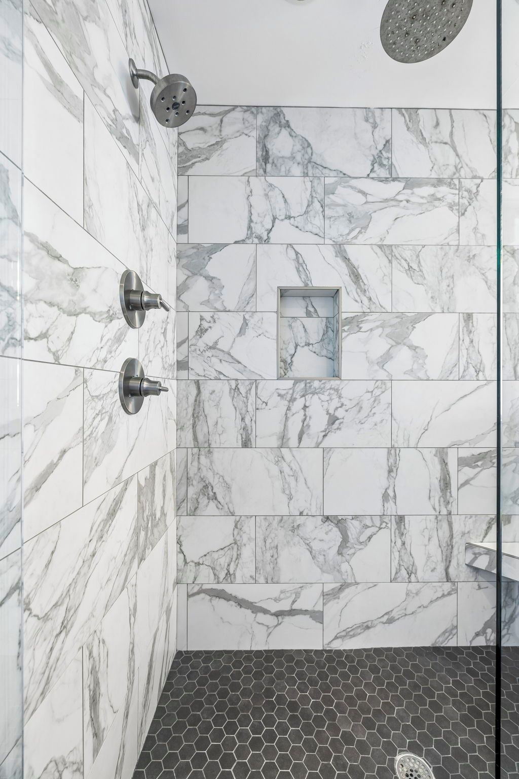 Une douche dotée d’un pommeau de douche à effet pluie, d’un pommeau de douche à main et d’un motif de carrelage hexagonal sur le sol.