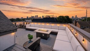 Une terrasse sur le toit, avec un canapé, une table et des guirlandes lumineuses.