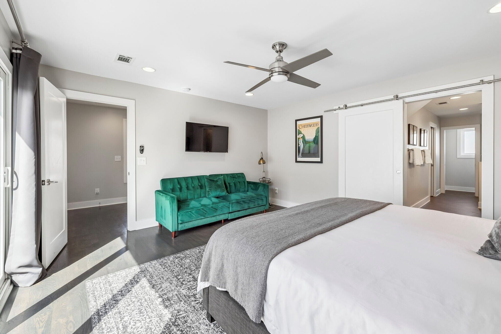 A bedroom with a bed, a ceiling fan, a green sofa, a TV, and a door leading to another room.