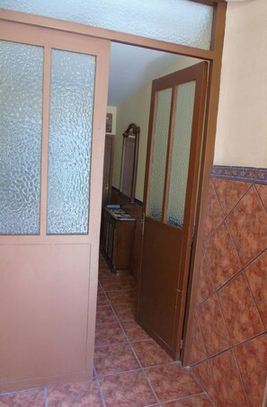A hallway with a wooden door, a mirror, and a tiled floor.