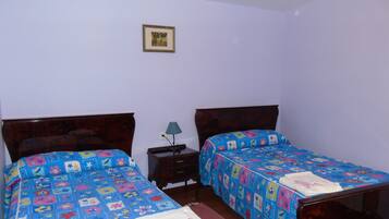 Een kamer met twee houten bedden, elk met een kleurrijke bloemenprint. Er staat een klein nachtkastje en aan de muur hangt een afbeelding in een lijst.