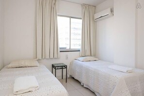 Una habitación con dos camas, una mesita y un equipo de aire acondicionado.