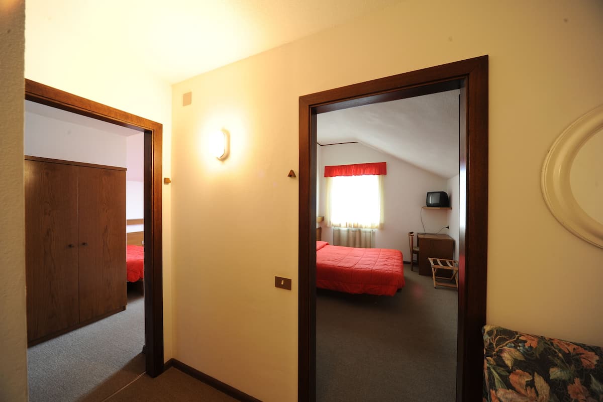 Ein Schlafzimmer mit Holzschrank, Bett mit roter Bettdecke, kleinem Tisch und Stuhl.