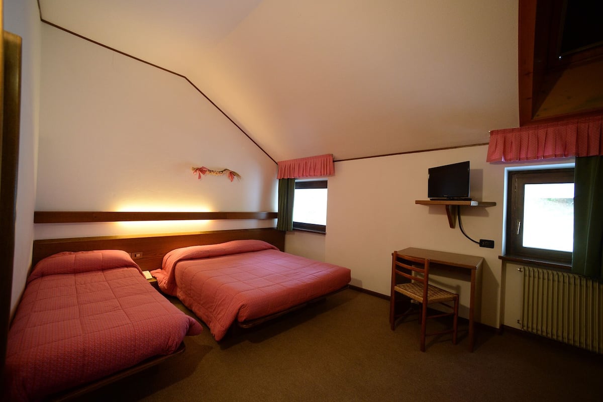 Ein kleines, gemütliches Zimmer mit zwei Betten, einem kleinen Tisch, einem Fernseher und einem Fenster mit Vorhängen.