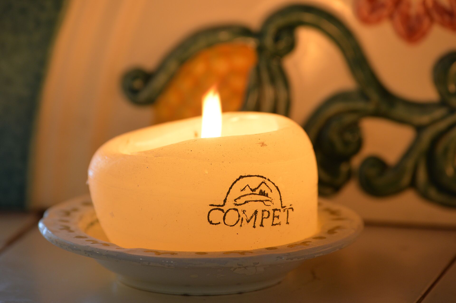 A lit candle with the word "COMPET" on a ceramic plate.
