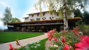 A hotel with a restaurant on the ground floor, outdoor seating, and a garden with red flowers. - Hotel Compet (Vignola-Falesina)