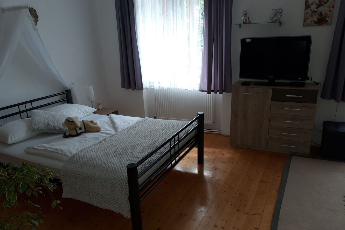 Un dormitorio con cama, televisión, cómoda y ventana con cortinas.