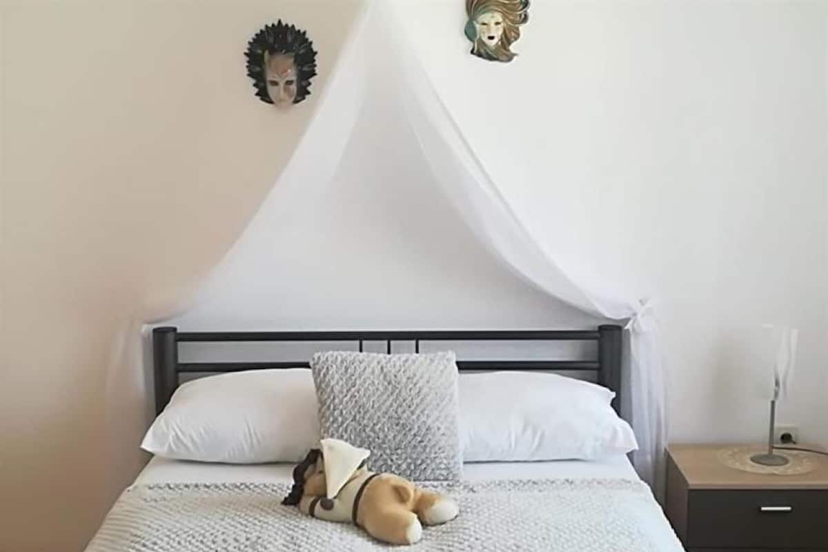 Una cama impecable con dosel blanco, un peluche y un adorno decorativo en la pared.