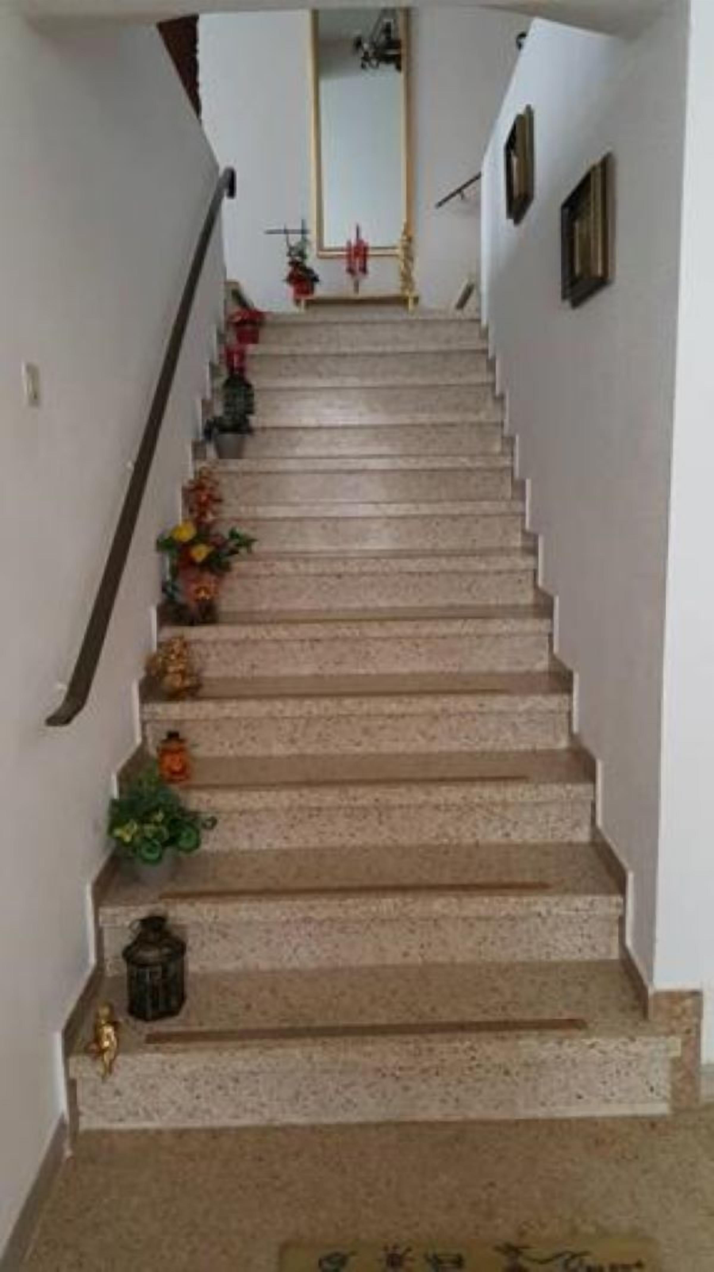 A staircase with a handrail on the left, leading to a landing with a mirror and a red object.