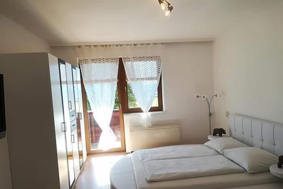 Un dormitorio con cama, mesita de noche, armario y ventana con cortinas.