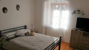 A bedroom with a bed, a bedside table, a lamp, a TV, and a window with curtains.