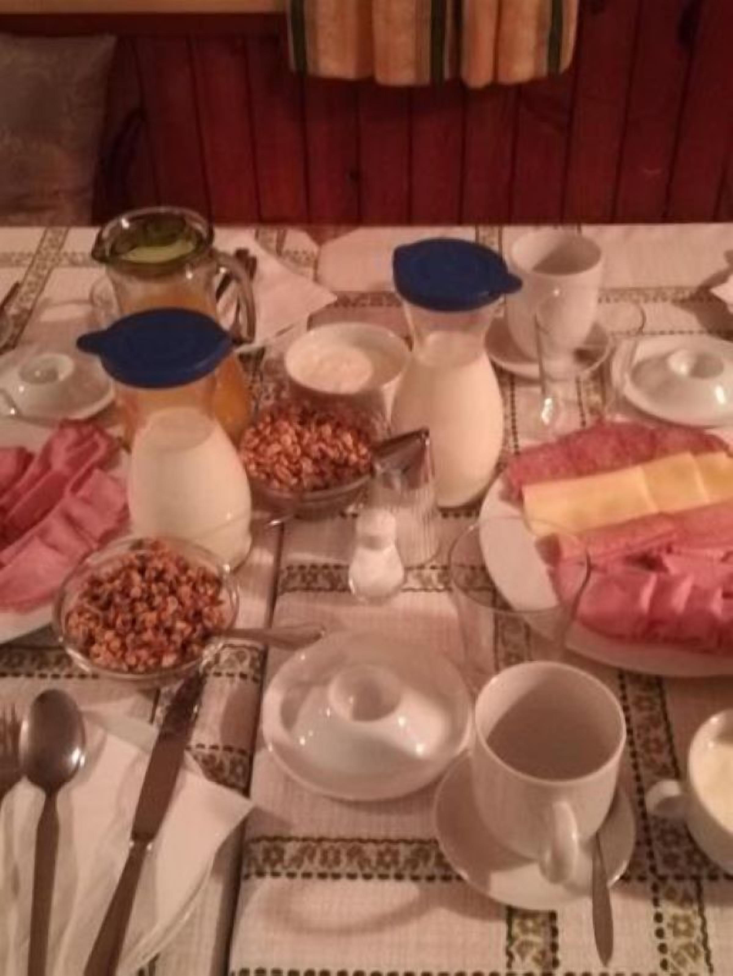 Una mesa de comedor dispuesta con diferentes platos, incluyendo un tazón de lentejas, una jarra de leche y un plato de jamón en rodajas.