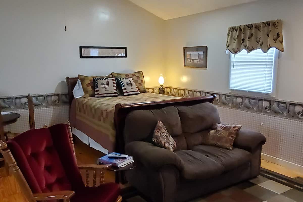 Una habitación con una cama, un sofá marrón, una mecedora de madera y un suelo a cuadros.