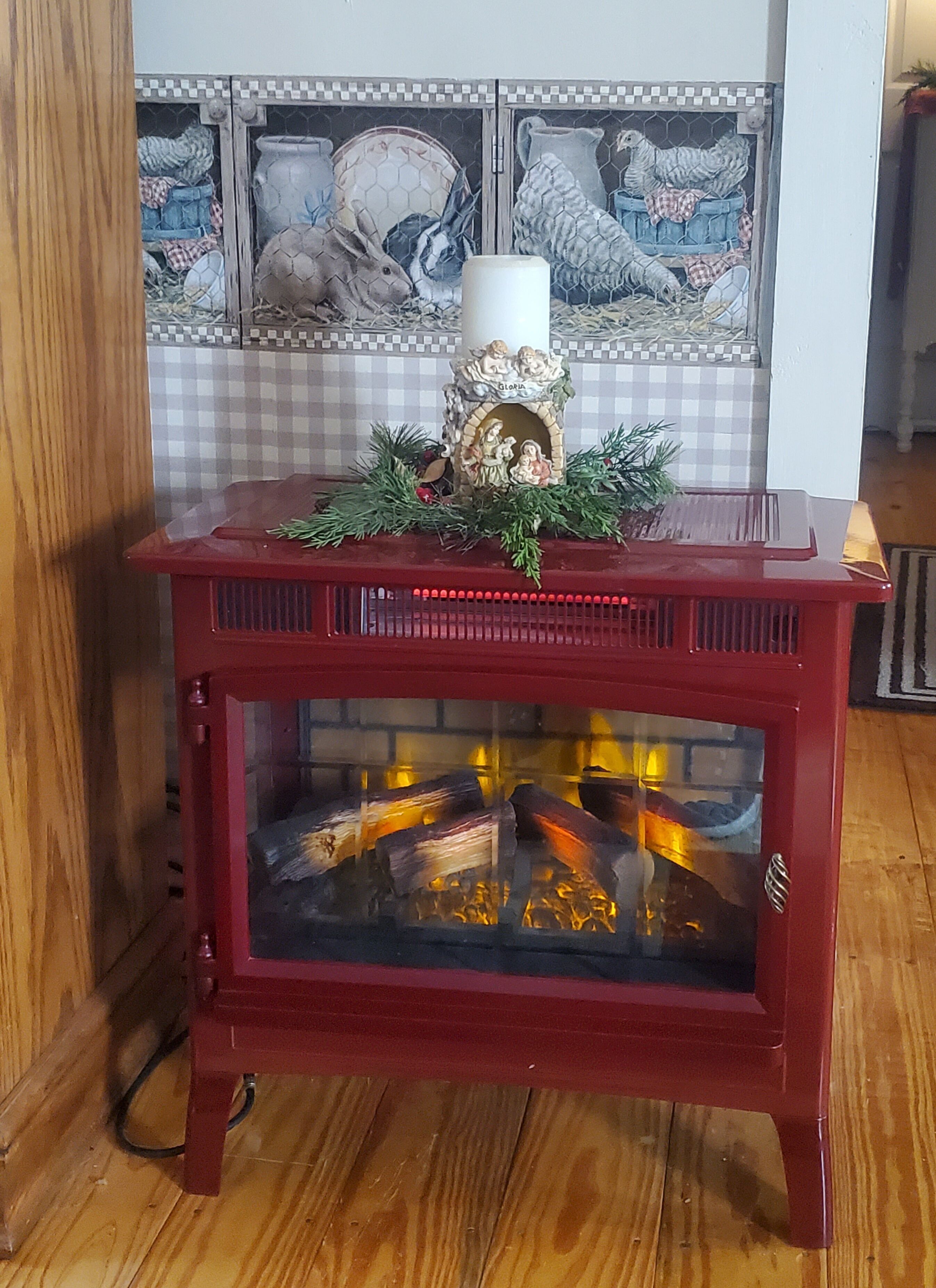A red wooden fireplace with a glass front, decorated with greenery and a nativity scene.