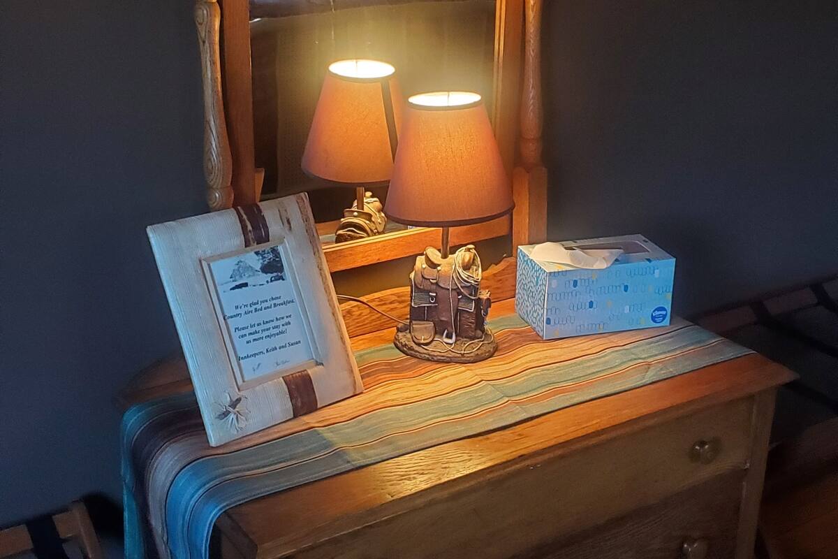 Un aparador de madera con un espejo, dos lámparas, una figurita, una nota enmarcada y una caja de pañuelos.