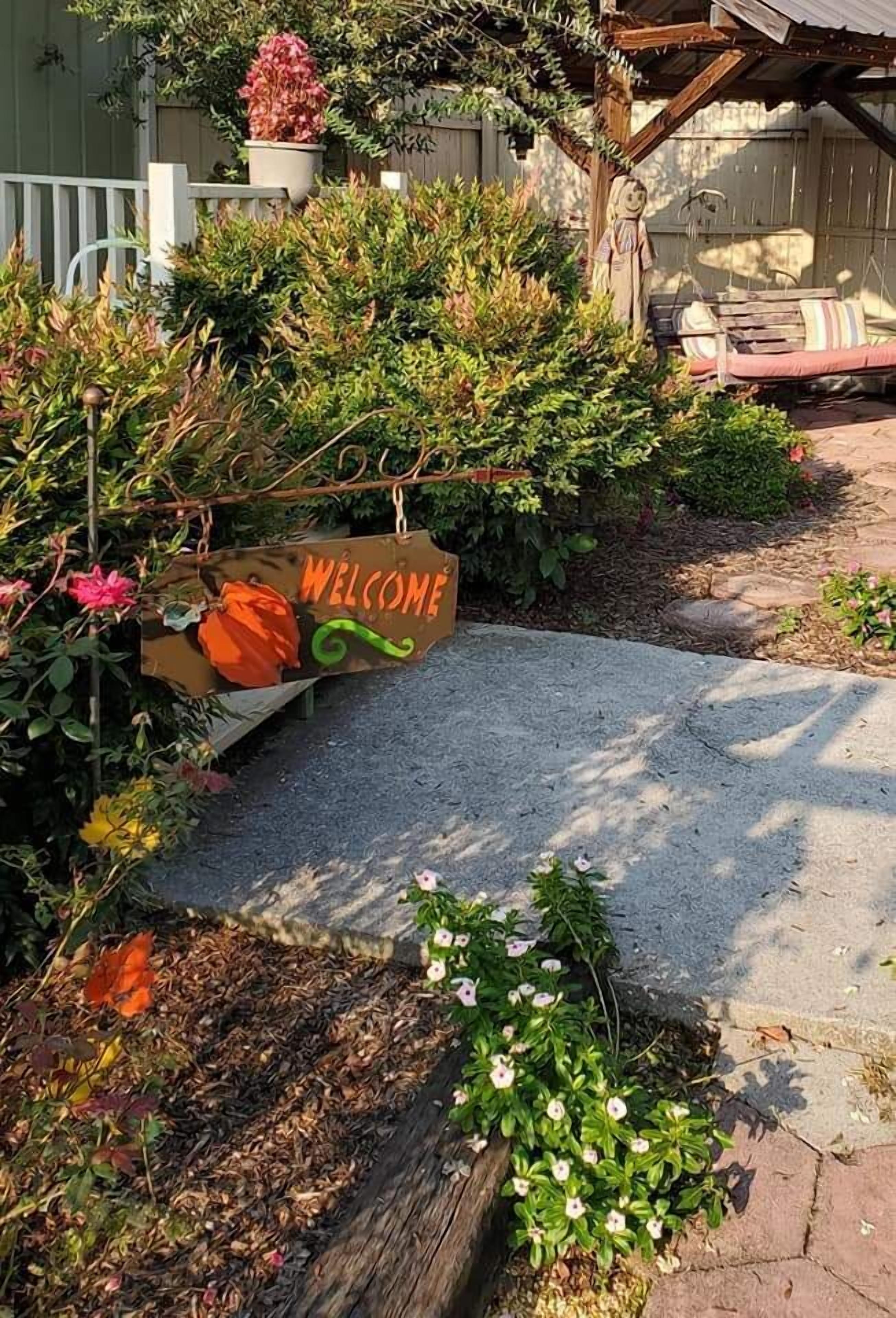 A welcome sign in a garden area with various plants and a bench.