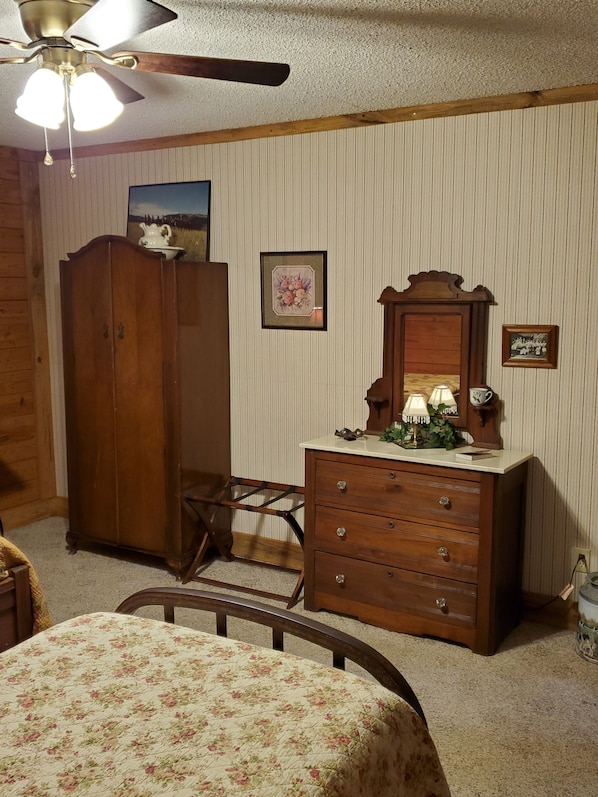 A bedroom with a wooden wardrobe, a bed with a floral bedspread, a dresser with drawers, a mirror, and a ceiling fan. - Country Aire Bed & Breakfast (Rock Spring)