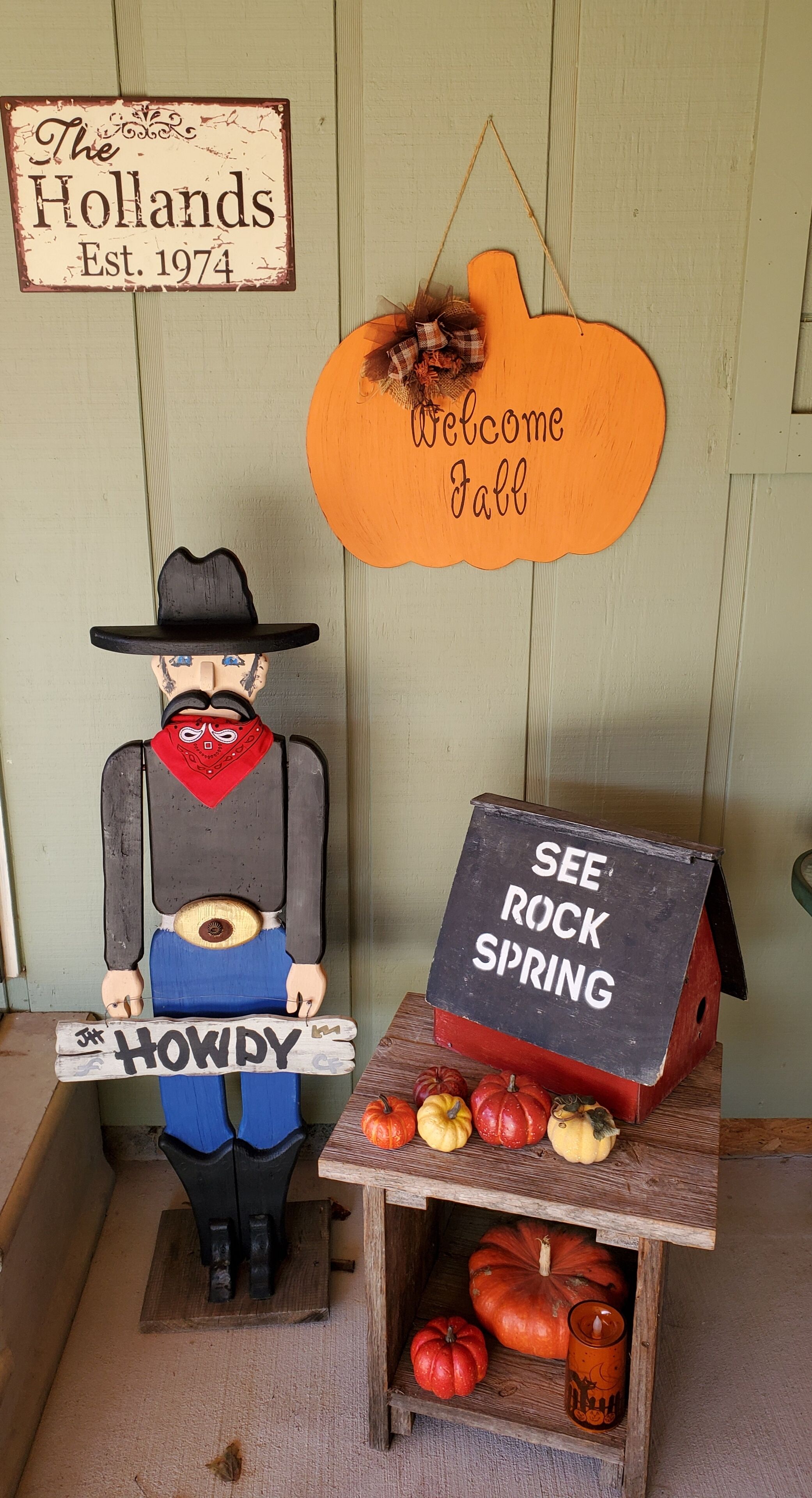 A rustic wooden figure holding a sign, a welcome sign, and a sign for rock spring.