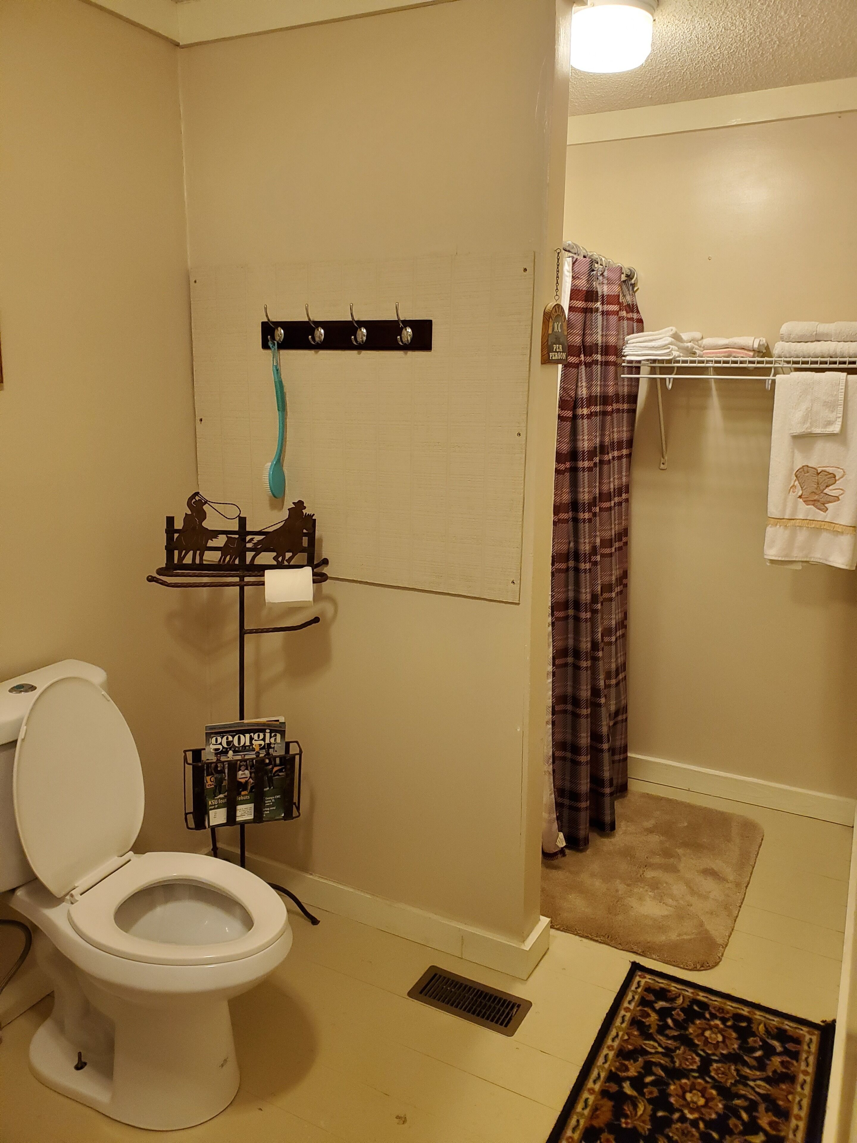 A bathroom with a toilet, a towel rack with folded towels, a shelf with toiletries, and a shower curtain.