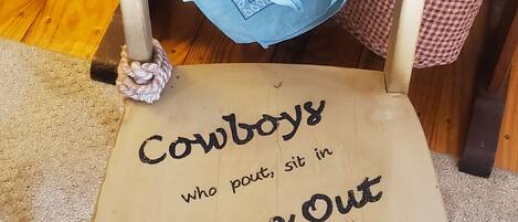 Una silla con sombrero vaquero y una bandana azul atada al respaldo. El asiento tiene el texto: 'Cowboys who pout, sit in Time Out'.