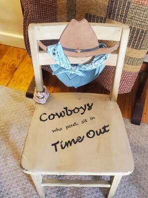 A chair with a cowboy hat and a blue bandana tied around the backrest. The seat has text that reads "Cowboys who pout, sit in Time Out." - Country Aire Bed & Breakfast (Rock Spring)