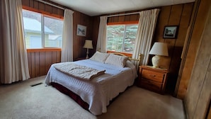 A bedroom with a large bed, wooden walls, two windows with curtains, a bedside table with lamps, and a framed picture on the wall. -  On Salmon River, quiet, private, house, where you can still see the milky way, (Salmon)