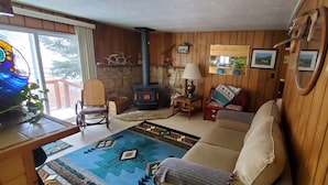A cozy living room with a sofa, a chair, a small table with a plant, a fireplace, and a large window. -  On Salmon River, quiet, private, house, where you can still see the milky way, (Salmon)