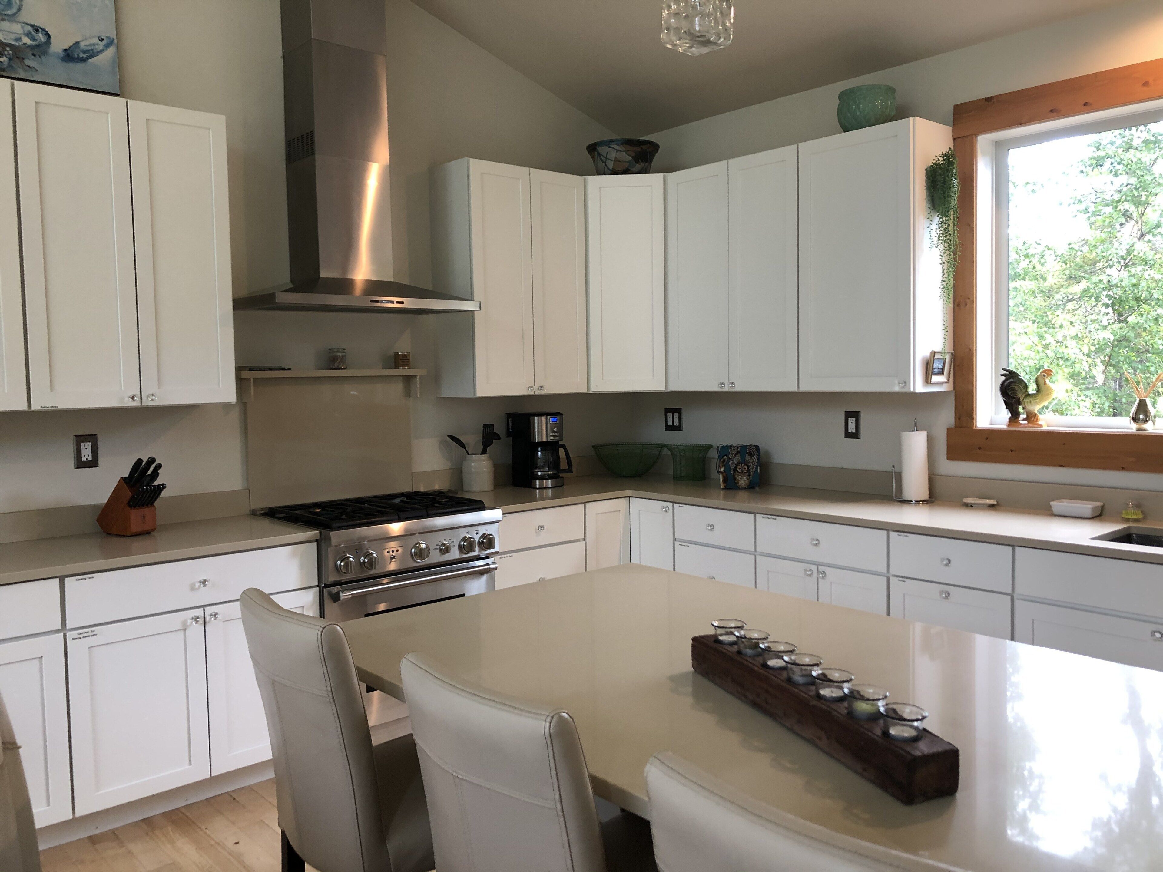 Une cuisine moderne avec des meubles blancs, une cuisinière en acier inoxydable et un grand îlot central agrémenté d’un porte-bougie.