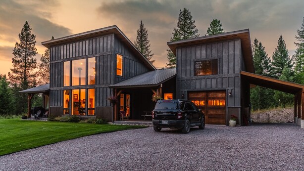 A modern two-story house with large windows and a gravel driveway.