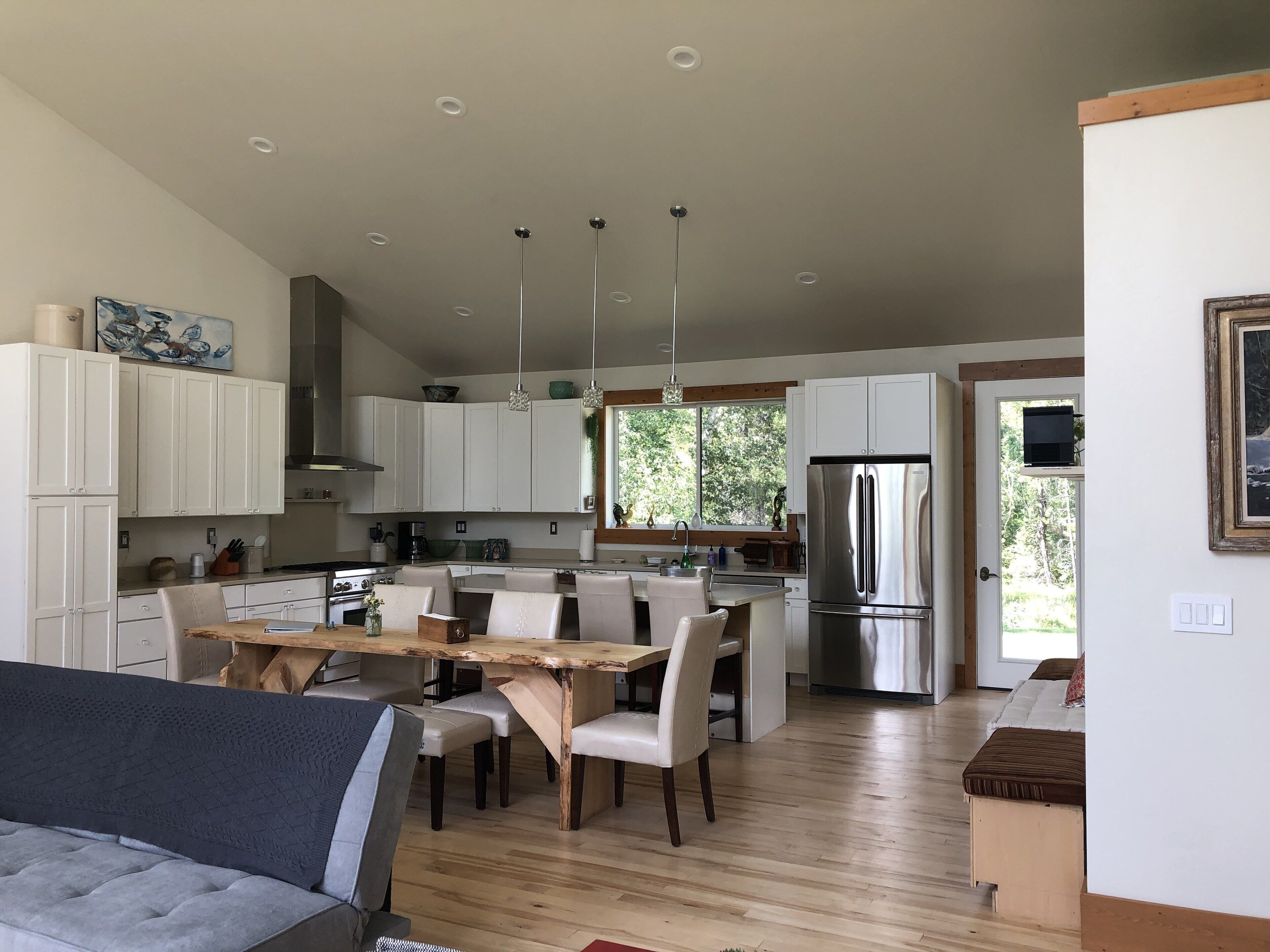 Une cuisine moderne avec des meubles blancs, des appareils en acier inoxydable et un coin repas comprenant une table et des chaises en bois.