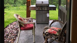 An outdoor patio with a grill, two wicker chairs with cushions, and a string of lights.