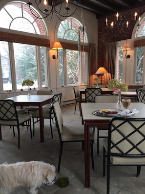 A dining area with tables and chairs, a chandelier, and large windows with curtains.
