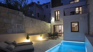 A modern outdoor pool area with a stone wall, a lounge with cushions, and a dining area with chairs and a table. - SANT SEBASTIA. Modern villa in Pollensa (Pollensa)