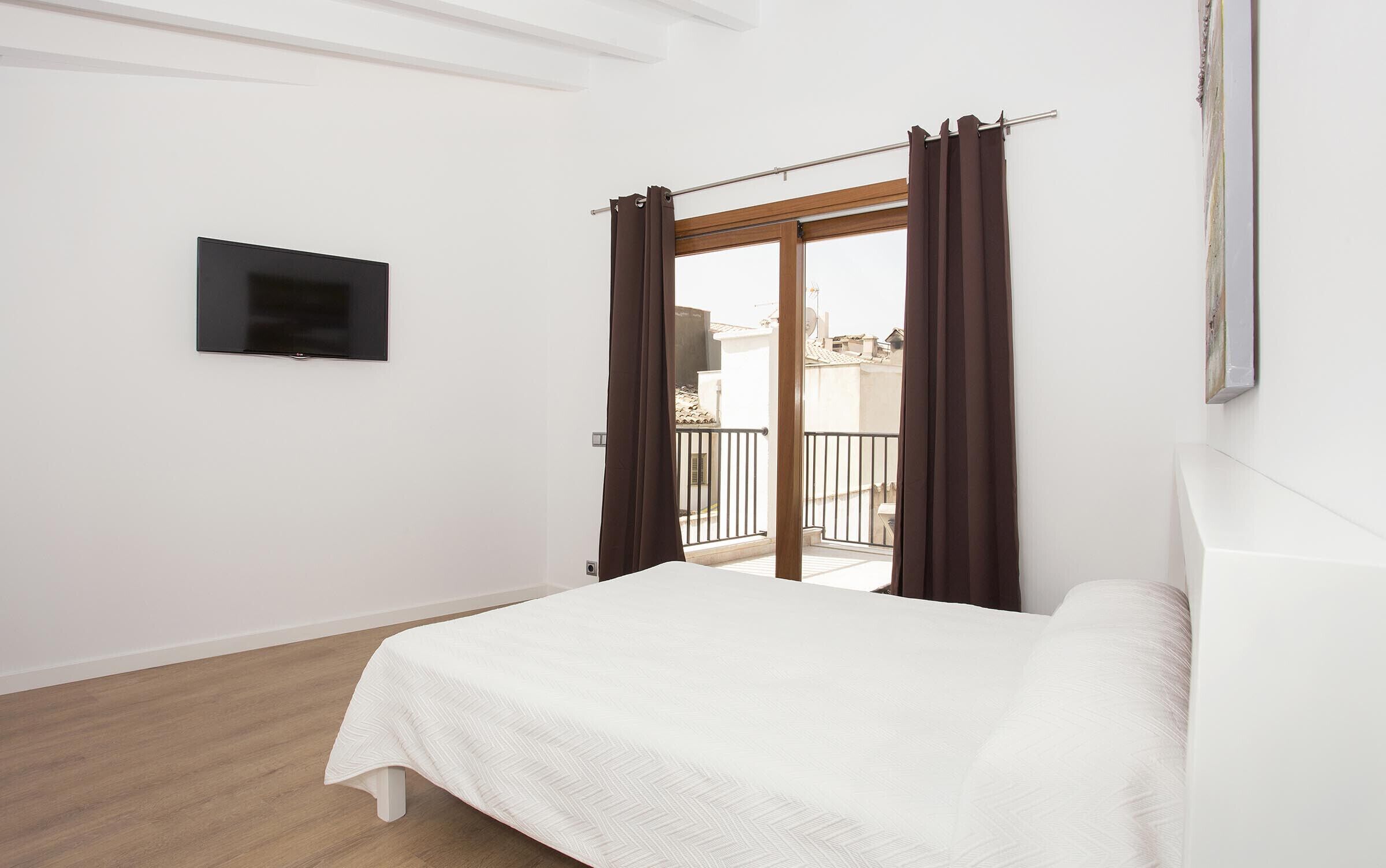 A bedroom with a bed, a TV mounted on the wall, and a balcony with curtains.