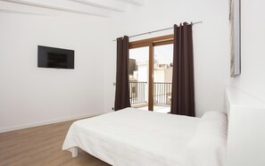Un dormitorio con cama, televisión montada en la pared y balcón con cortinas.