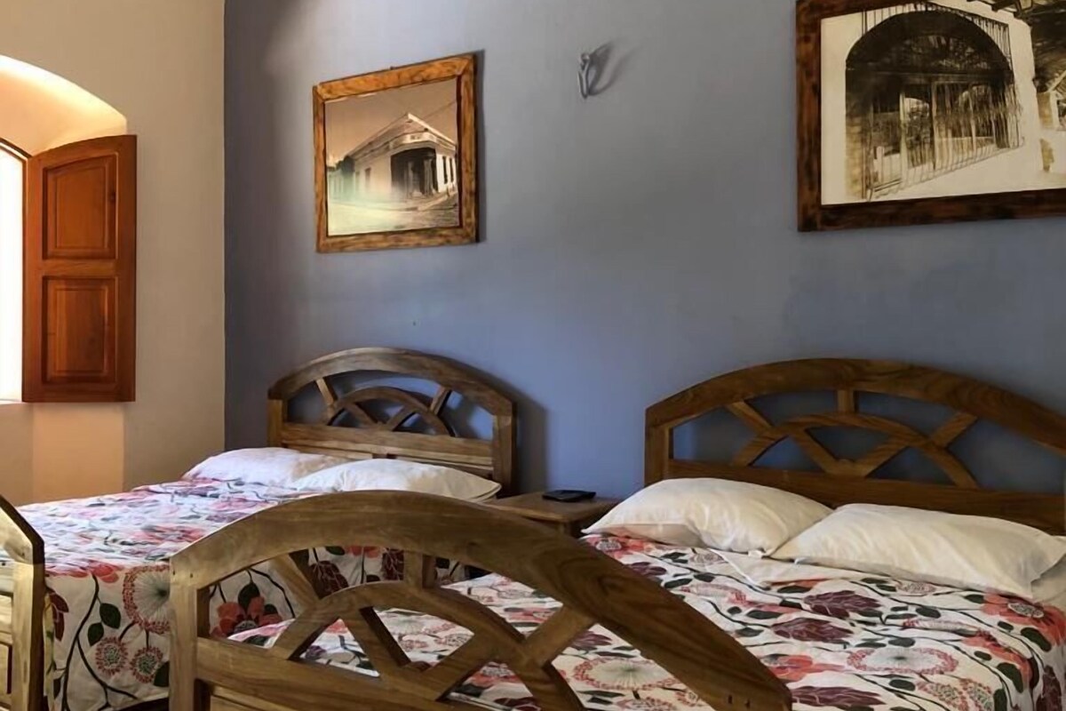 A room with two wooden beds with floral bedding, a wooden cabinet, and two framed pictures on the wall.