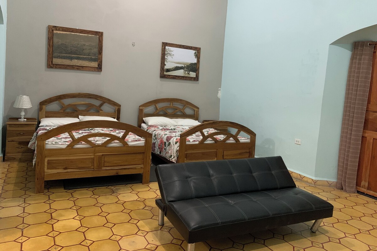 A bedroom with two wooden beds, a black leather sofa, and hexagonal patterned flooring.