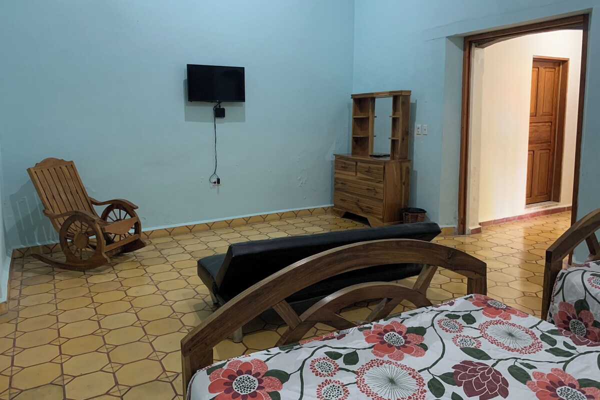A bedroom with a bed, a wooden chair, a dresser, and a television mounted on the wall.