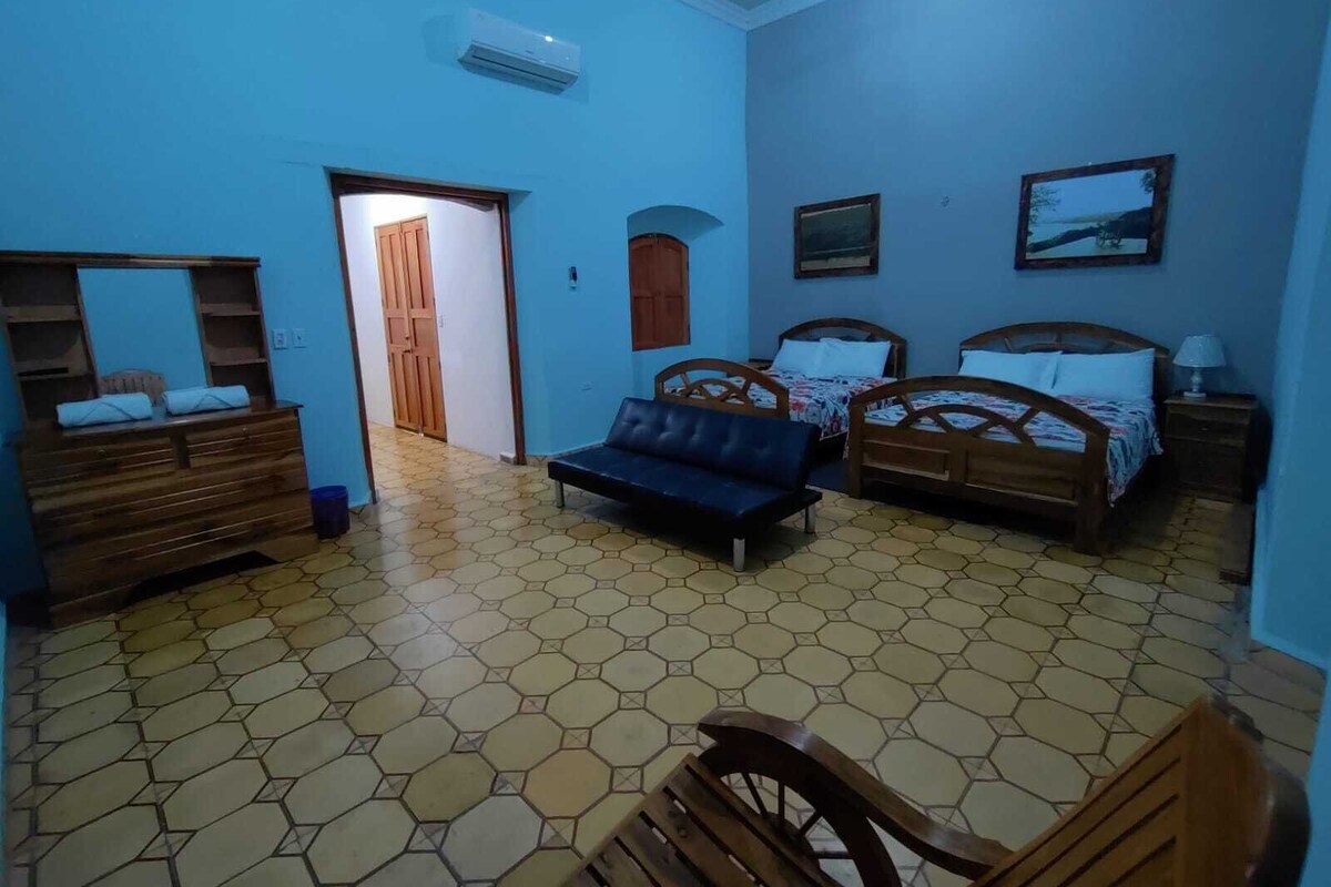 A room with two wooden beds, a sofa, a wooden dresser, and a tiled floor.