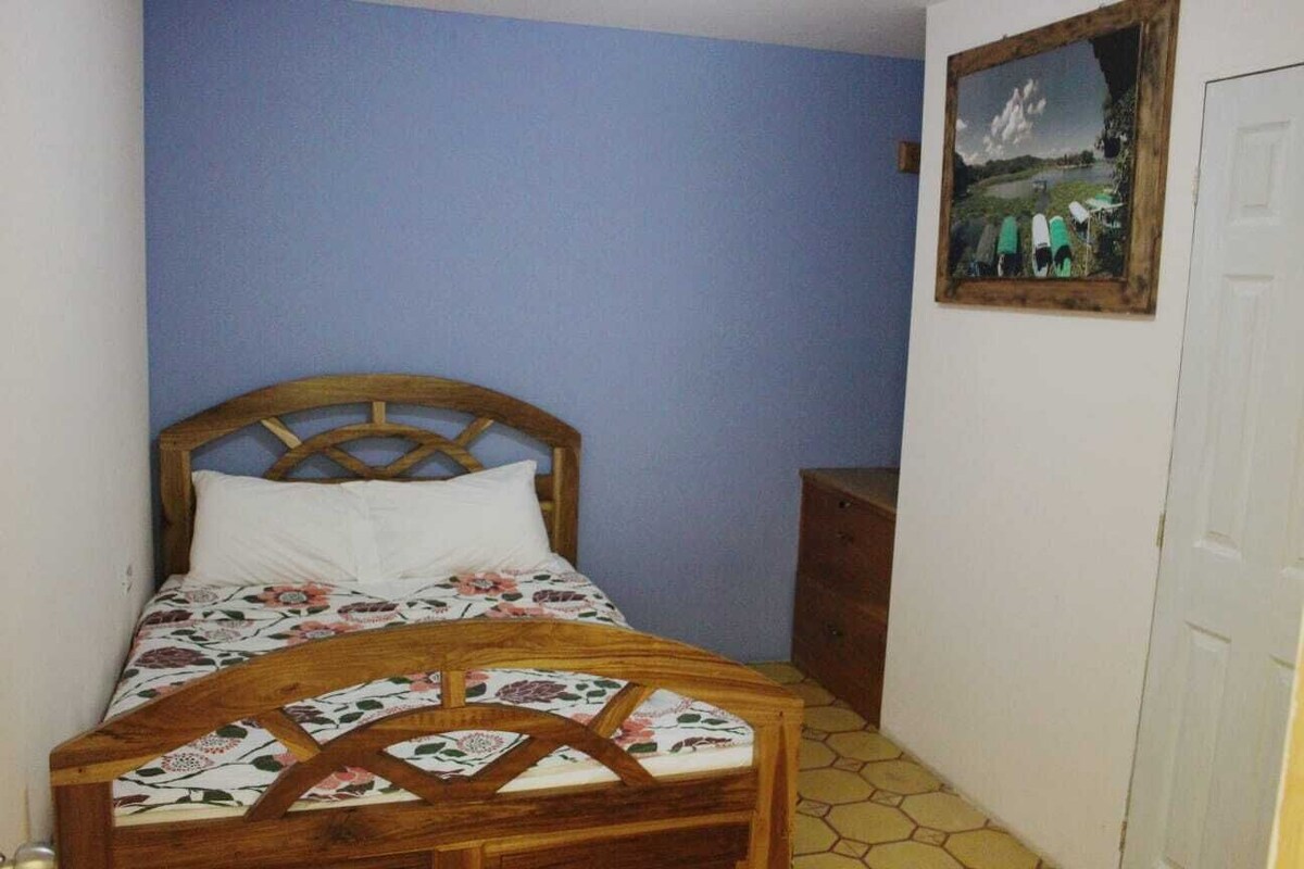 A bedroom with a wooden bed, floral bedding, a small wooden cabinet, and a framed picture on the wall.
