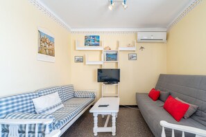 Una sala de estar con un sofá, una mesa de centro, un televisor y estantes en la pared.
