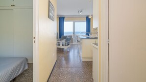 Une chambre d’hôtel comprenant un lit, une kitchenette, un coin repas avec une table et des chaises, et une vue sur la mer par une grande fenêtre.